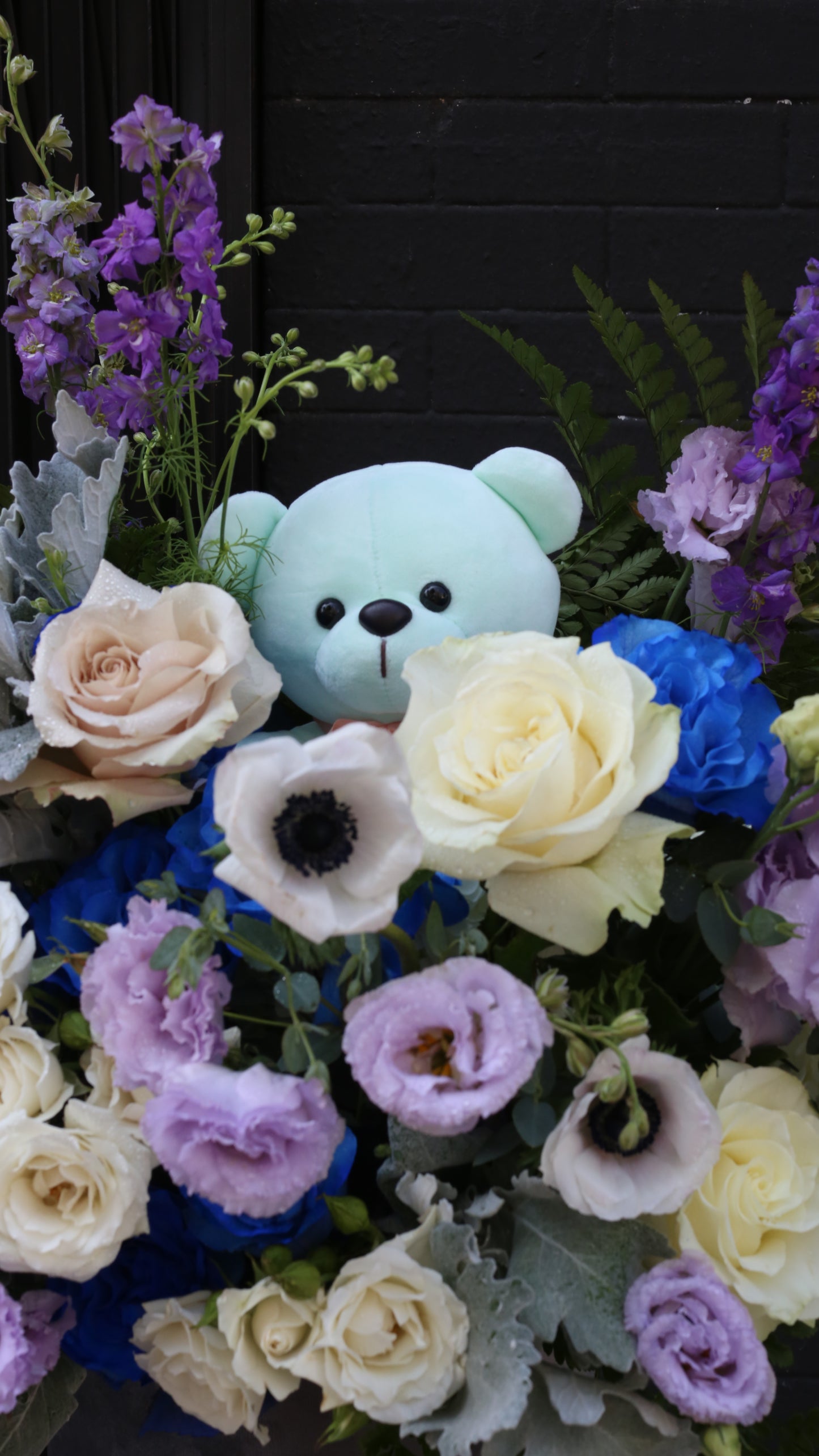 Full view of the Baby Blossom arrangement showcasing rich blue tones, textured petals, and lush greenery.