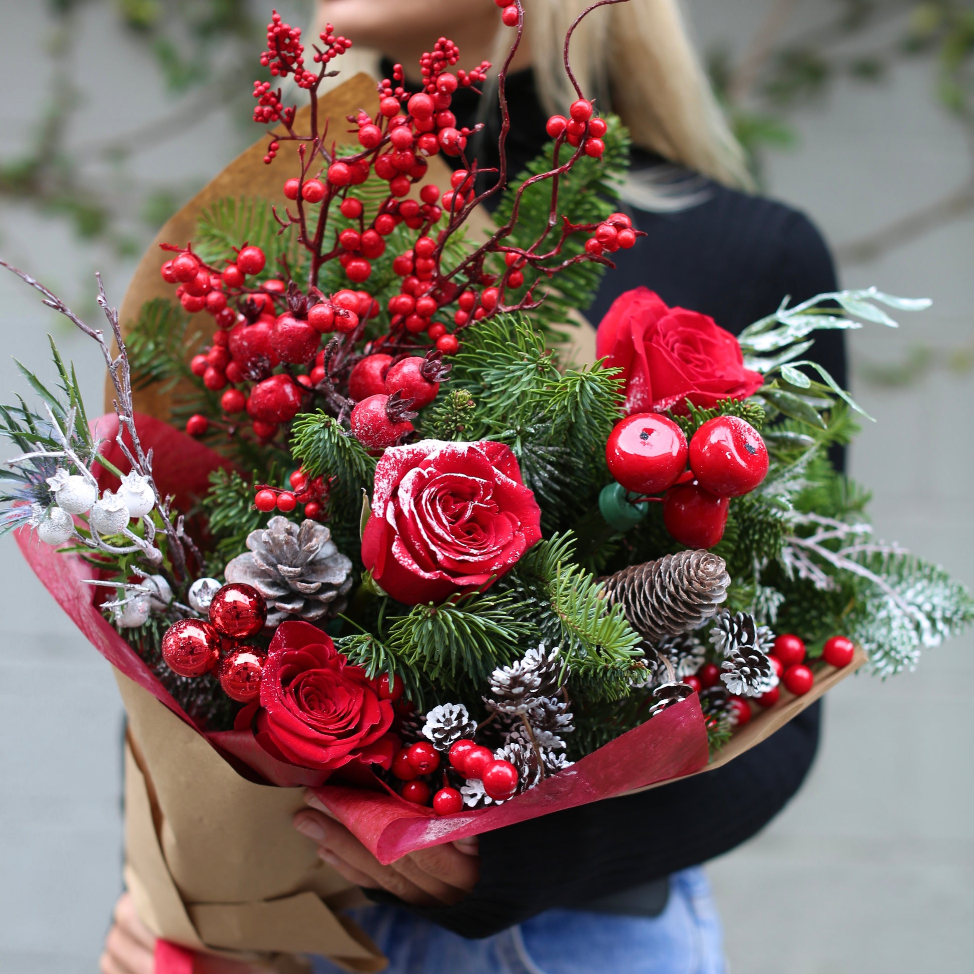 Festive Christmas bouquet featuring red roses, pine branches, and pinecones arranged in a decorative style with a holiday toy accent