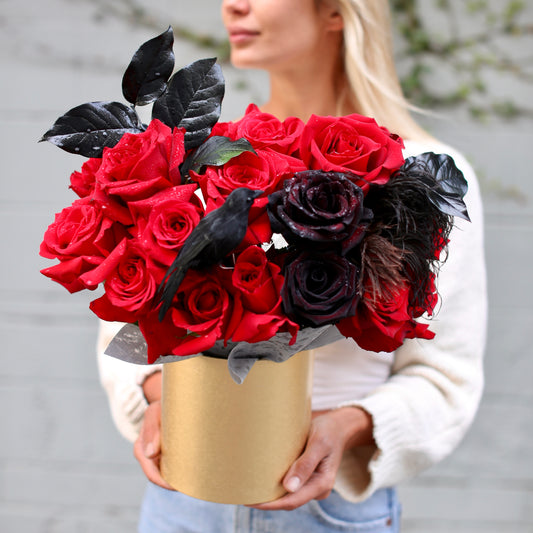 Dramatic Halloween bouquet featuring red roses, black blooms, feathers & raven decor in a luxury keepsake box – ideal for premium gifting