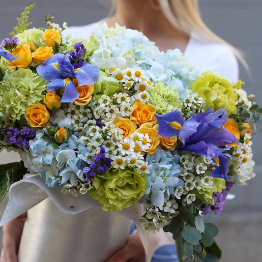 Vibrant floral arrangement featuring yellow roses, hydrangeas, carnations and irises in a decorative spring-themed box