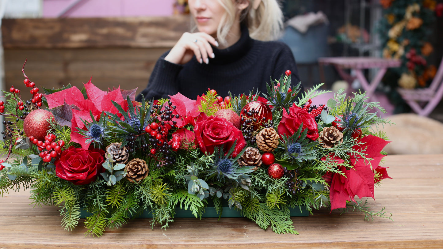 Elegant Christmas centerpiece featuring white roses, pinecones, and festive greenery arranged in a decorative holiday style