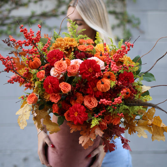 Luxurious autumn bouquet featuring red roses, dahlias, berries and mini pumpkins in a full, elegant arrangement
