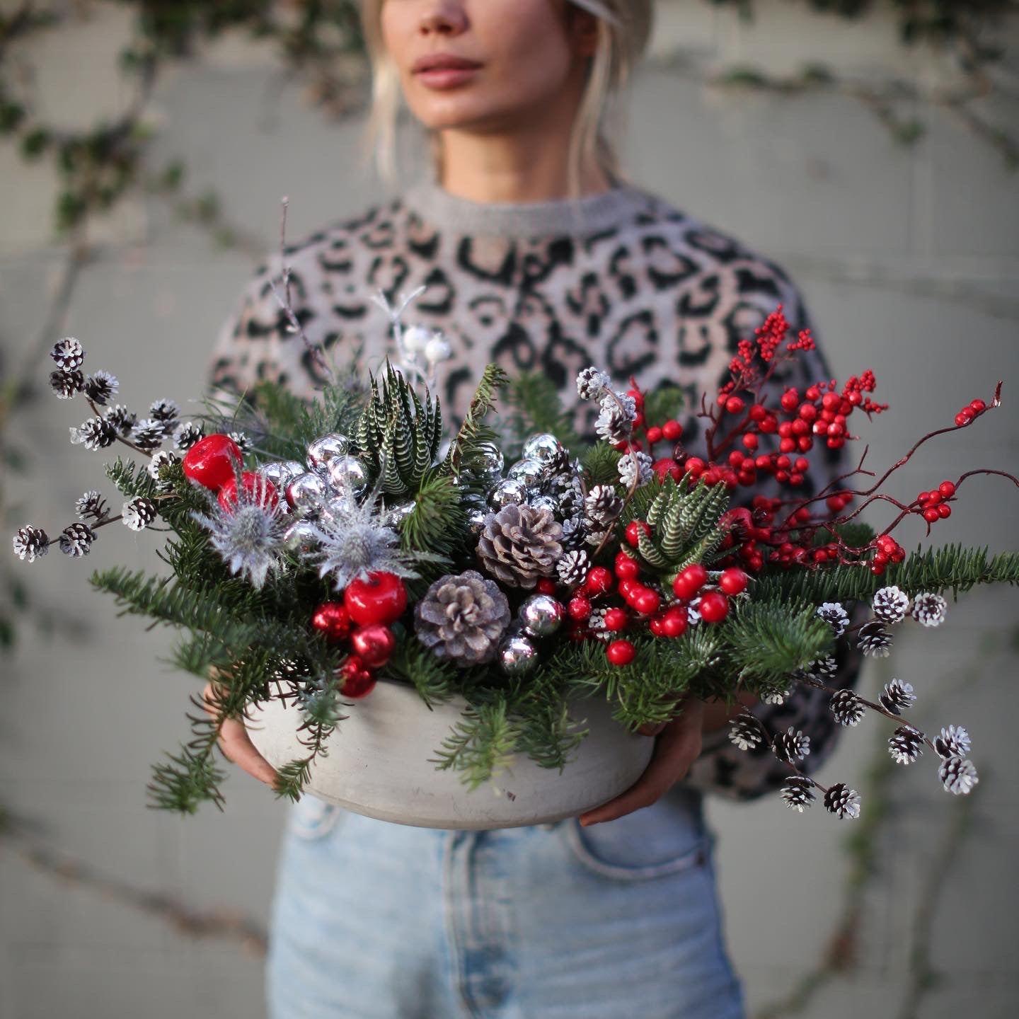 Festive floral arrangement showcasing silvery pinecones, blue thistle and lush greenery in a celebratory winter-inspired design